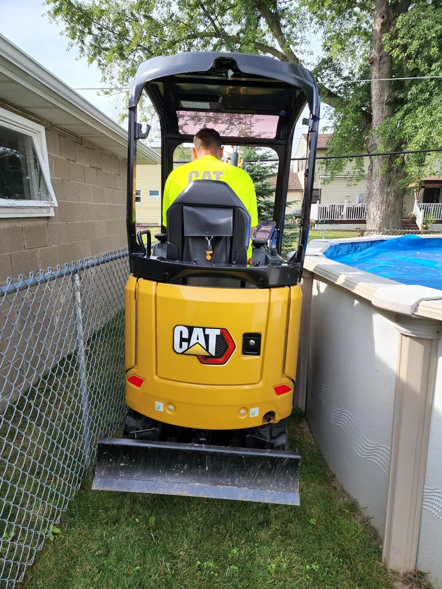 CAT excavator navigating narrow Cheektowaga backyard between fence and pool