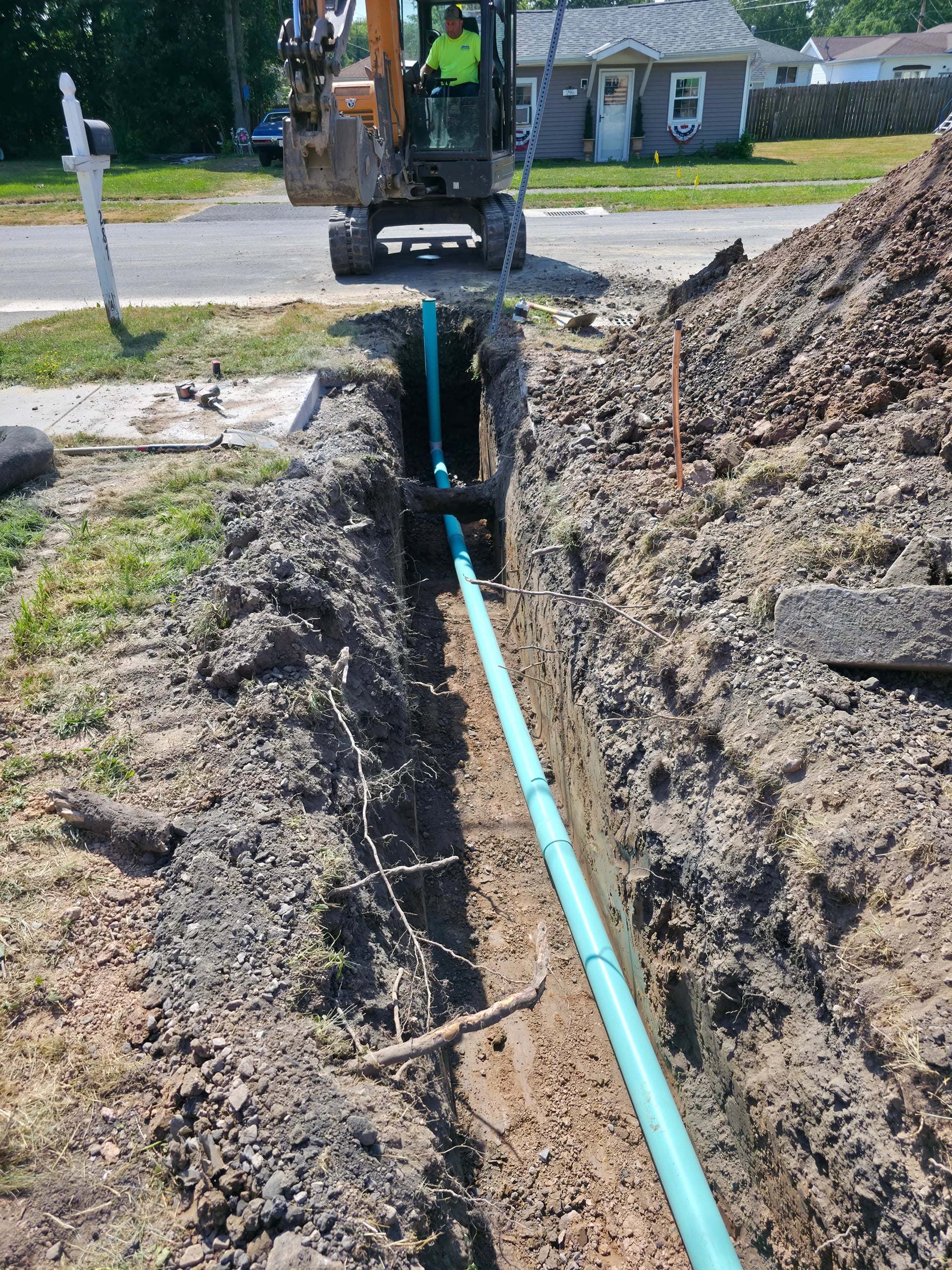 Mini excavator digging sewer trench in WNY residential yard with blue PVC pipe