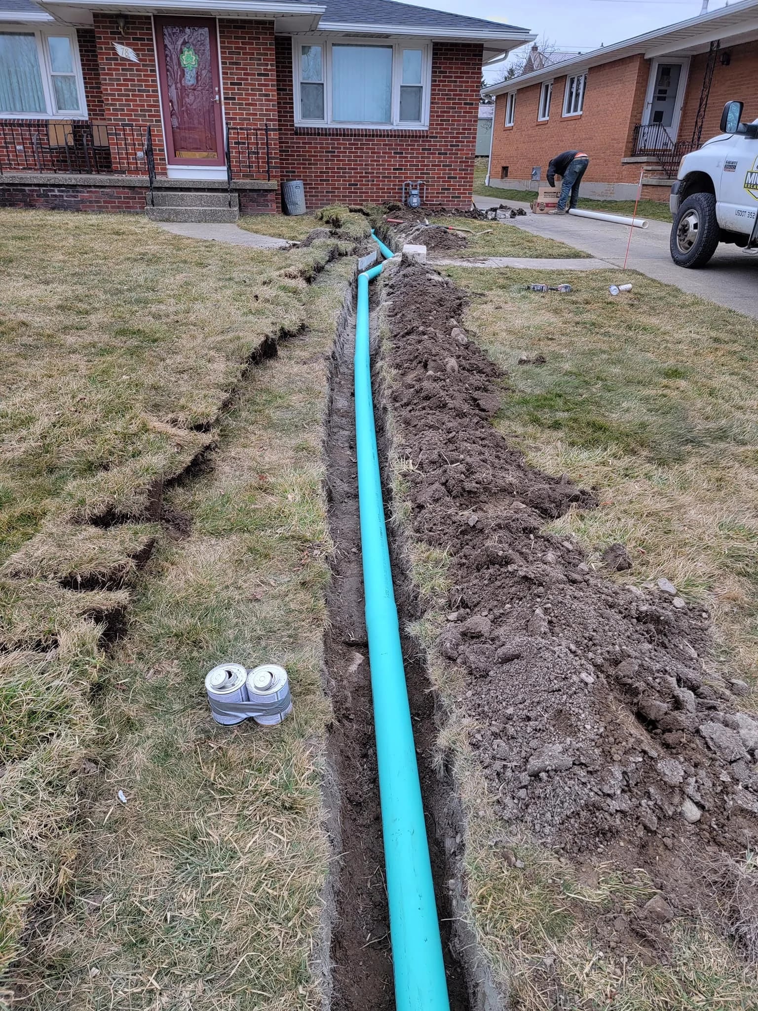 PVC sewer trench at brick Buffalo house with worker and truck at sidewalk